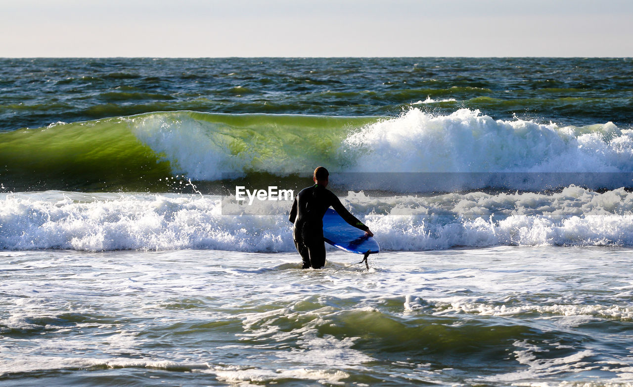 Rear view of surfer with surfboard standing in sea