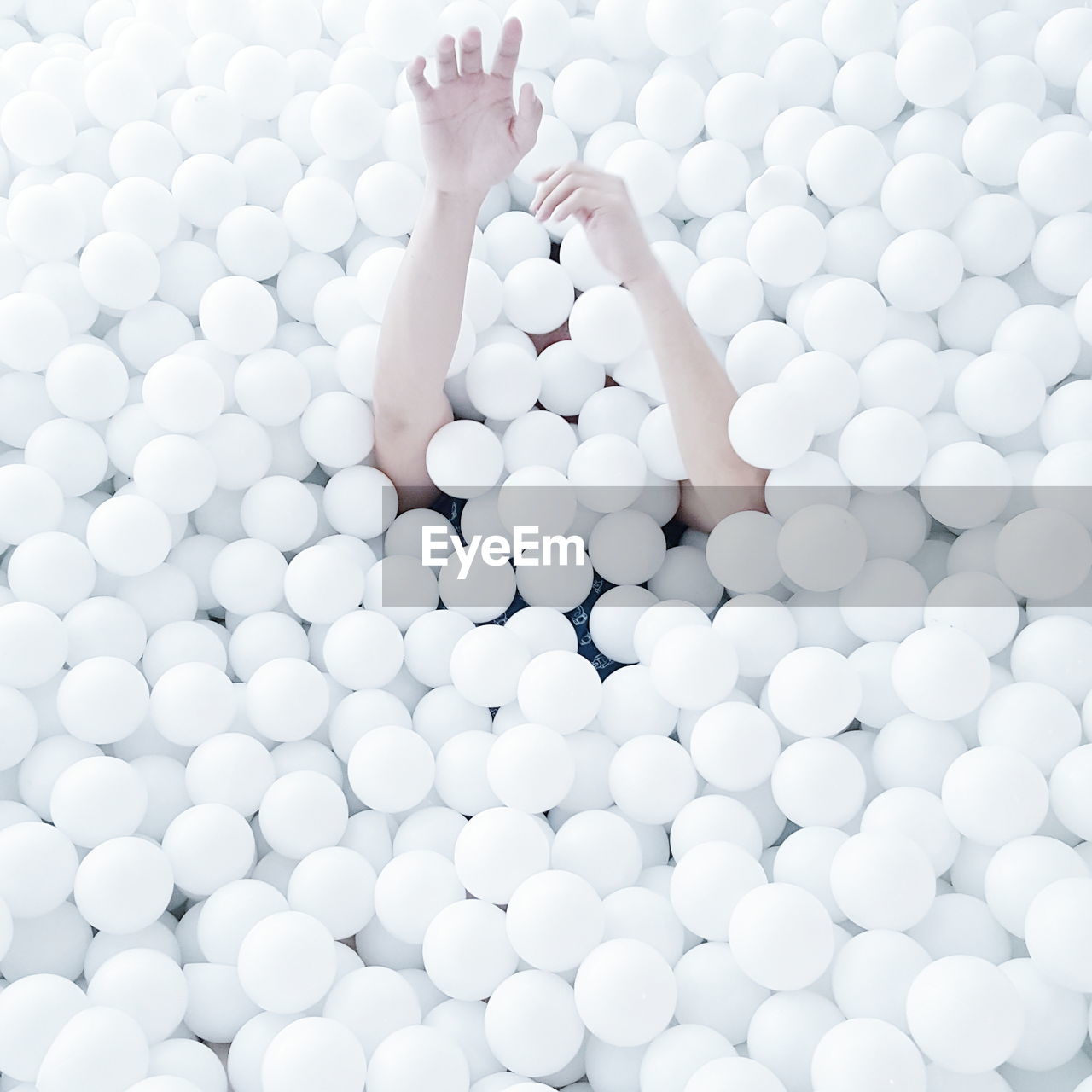 Cropped image of hand emitting from white ball pool