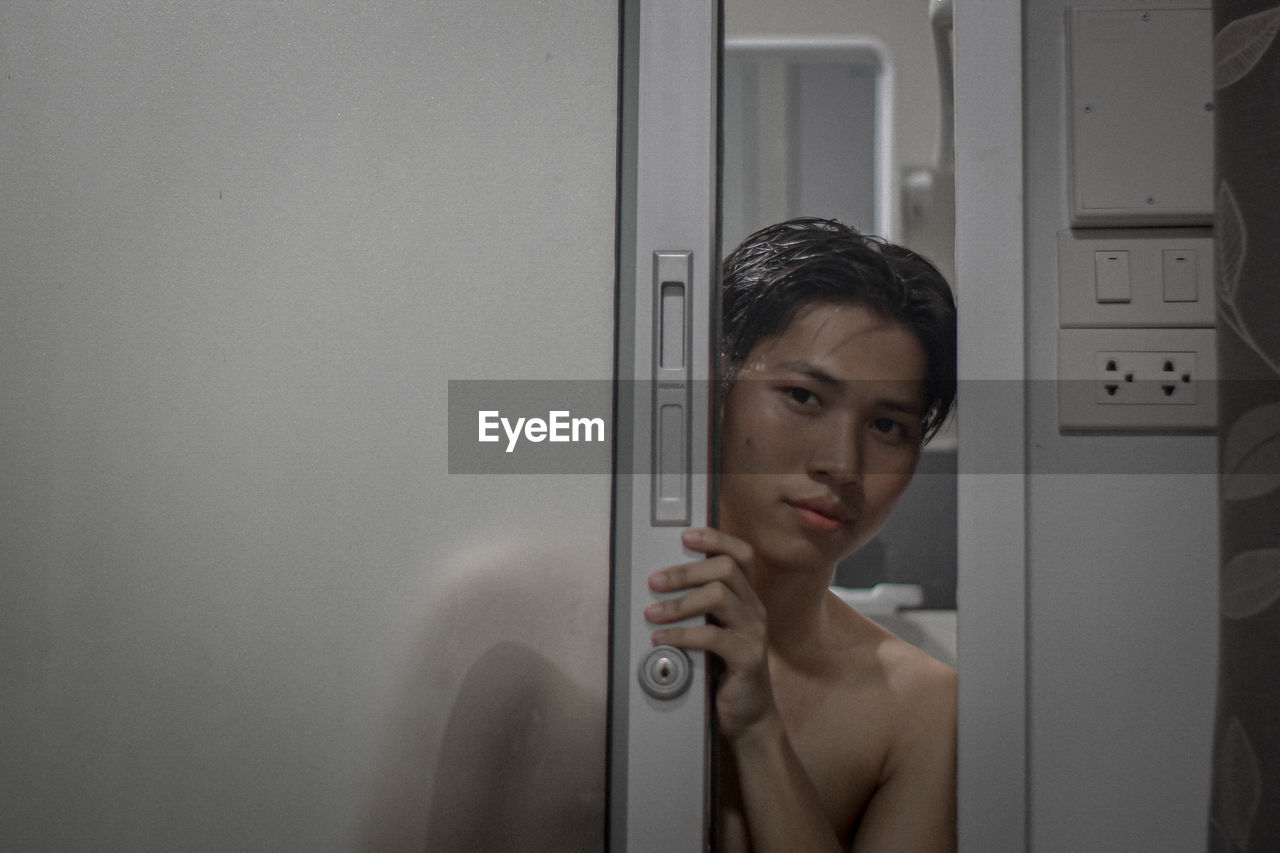 Portrait Of Shirtless Young Man Looking Through Door On Eyeem