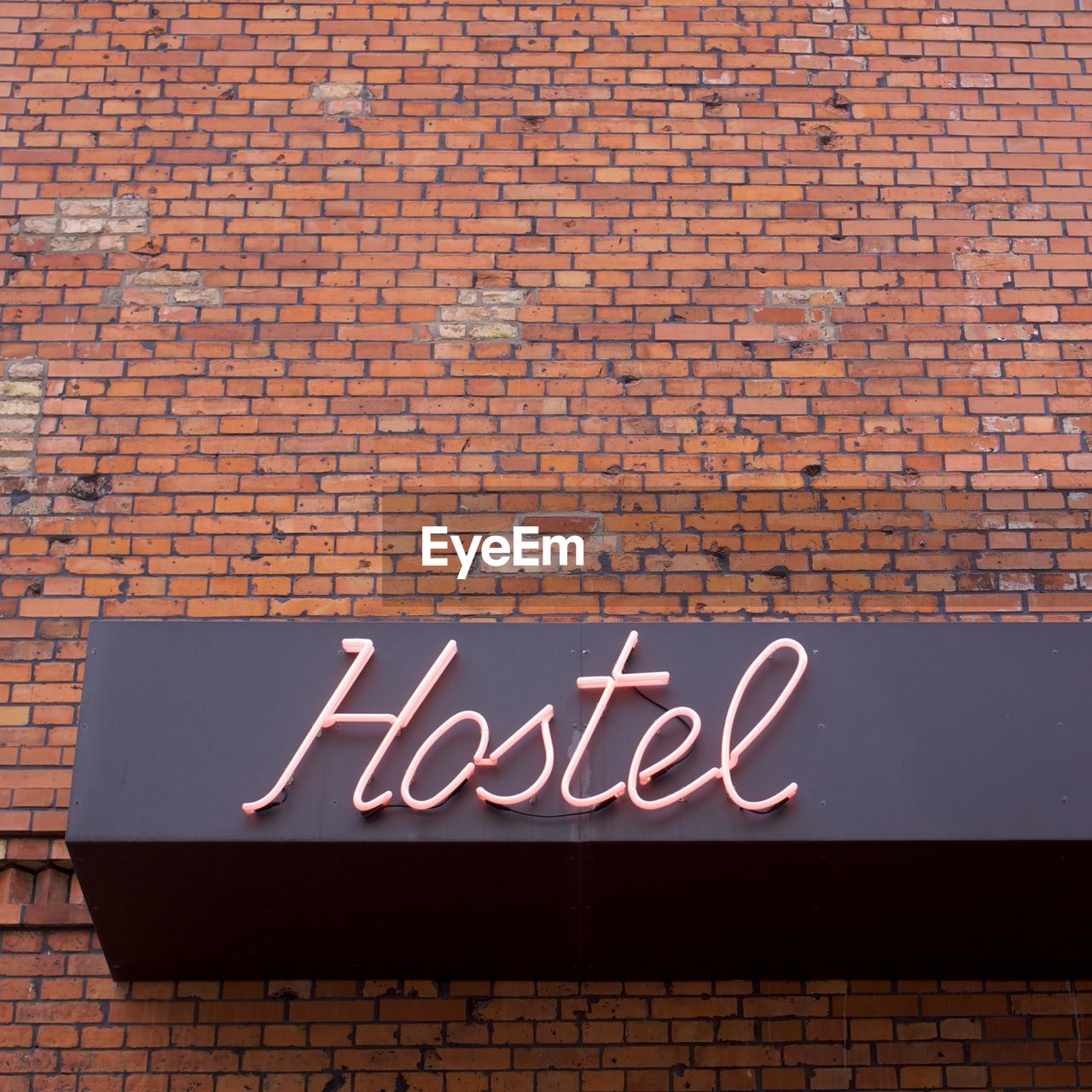 Low angle view of neon hostel sign on brick wall