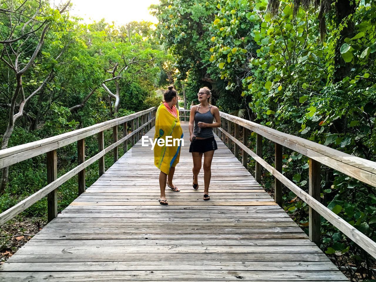 Female friends walking on wooden bridge amidst trees