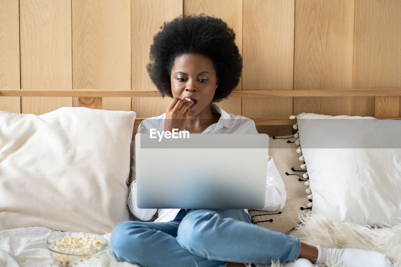 Young woman using laptop while sitting on bed