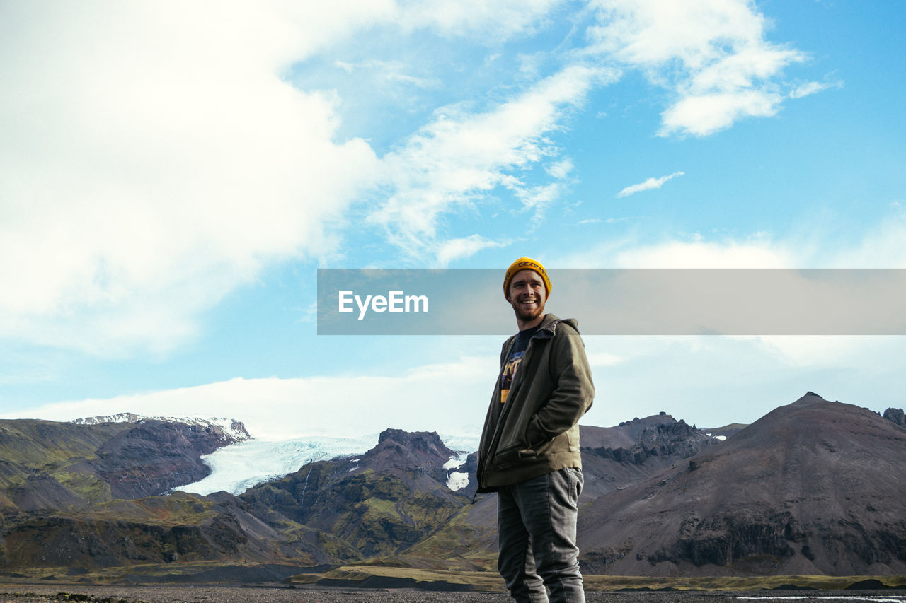 Smiling man standing by snowcapped mountain against sky