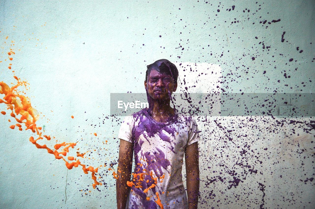 Man standing amidst splashing paints against wall