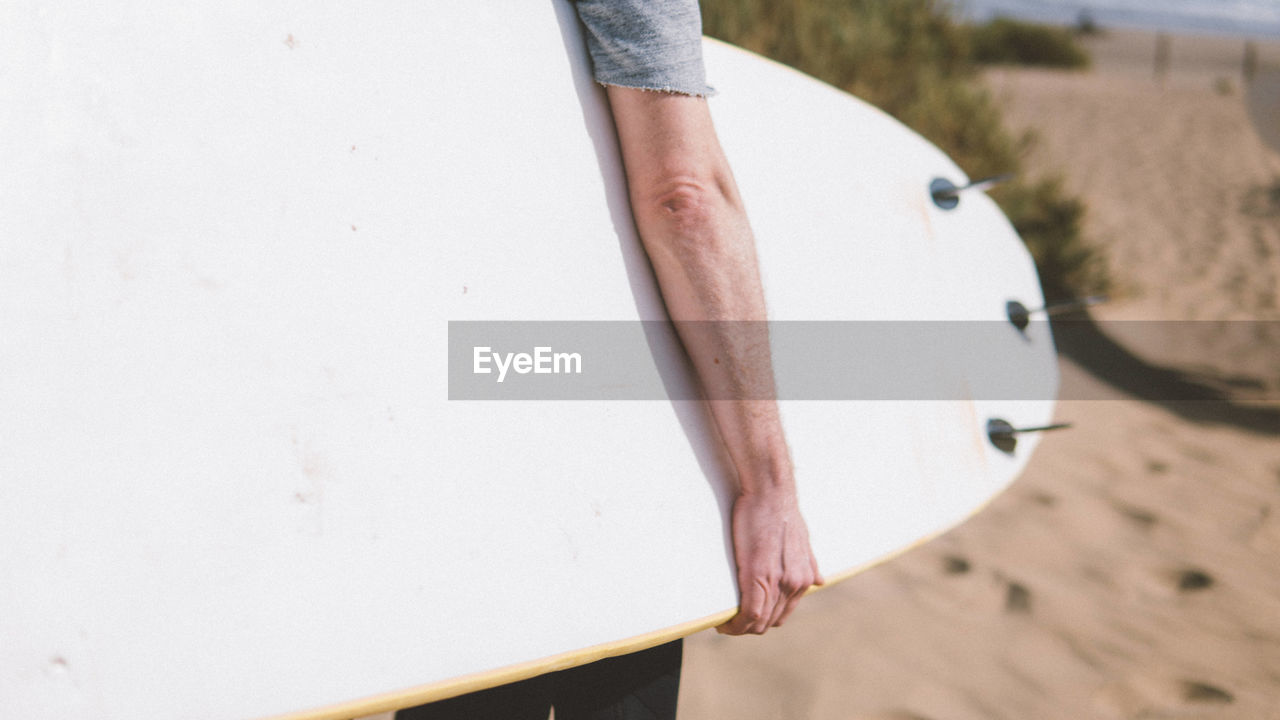 Midsection of man holding surfboard at beach