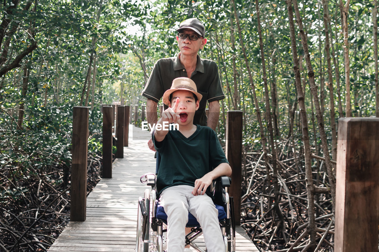 Father with disabled boy on wheelchair against trees