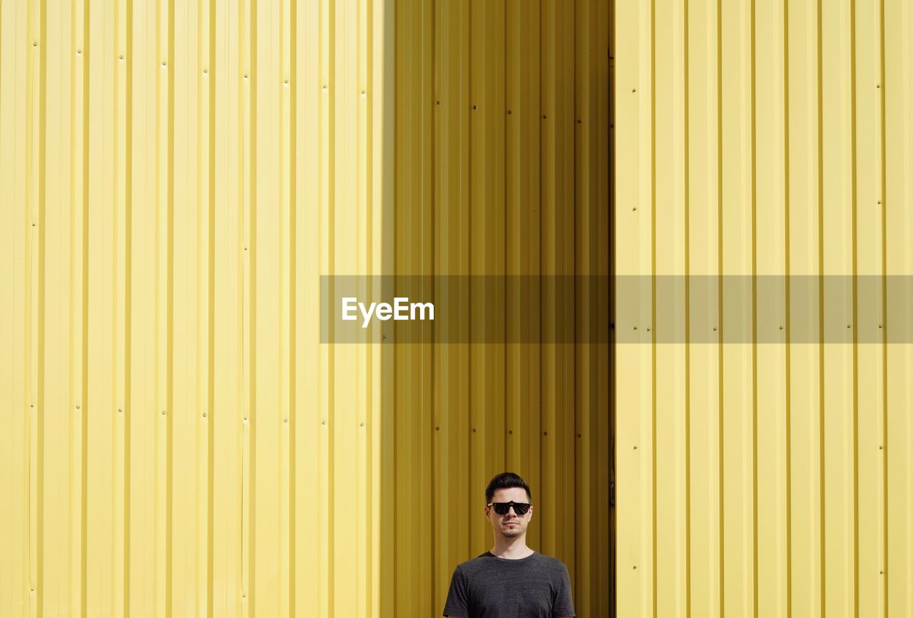 Portrait of man wearing sunglasses against yellow corrugated iron