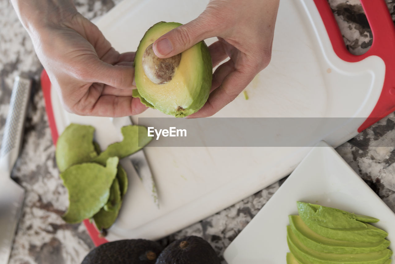 Cropped image of hands peeling avocado on cutting board