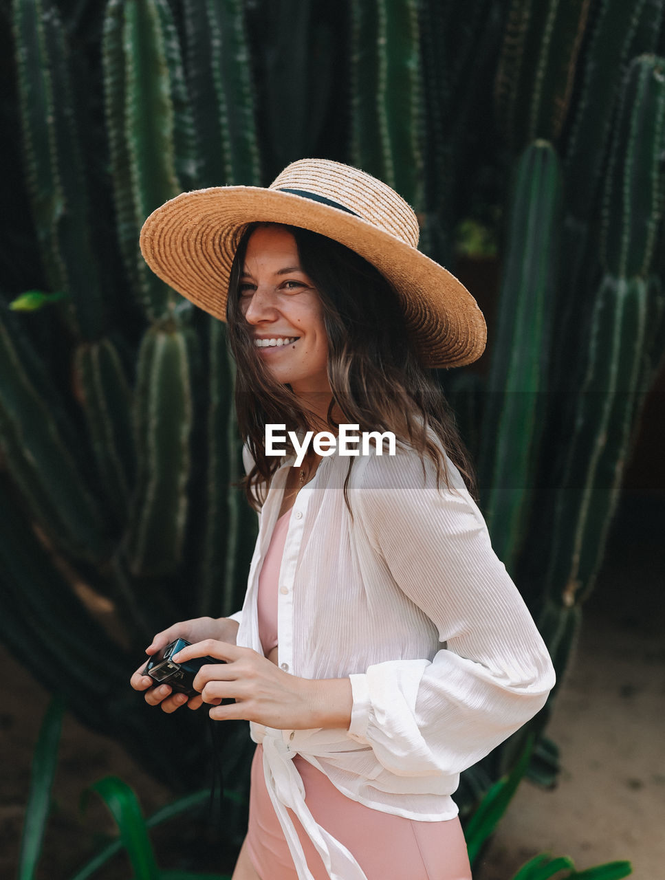 Smiling woman wearing hat while walking by plants