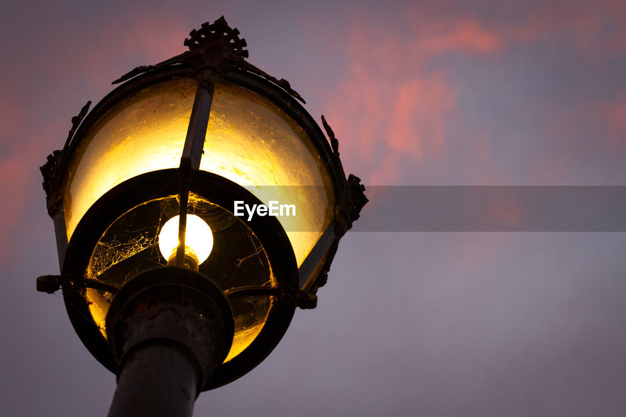 LOW ANGLE VIEW OF ILLUMINATED STREET LIGHT AGAINST SKY AT DUSK