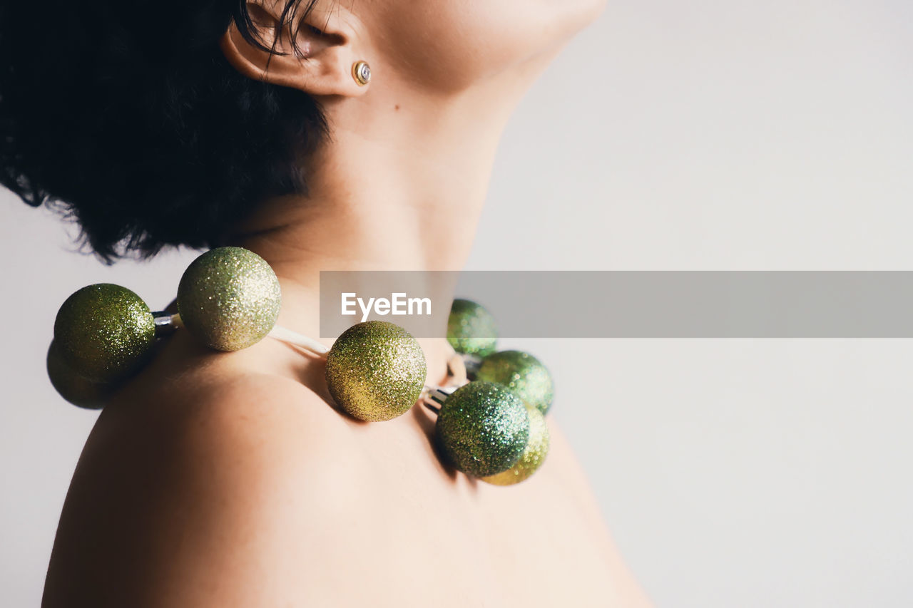 Midsection of topless mature woman wearing green necklace against white background