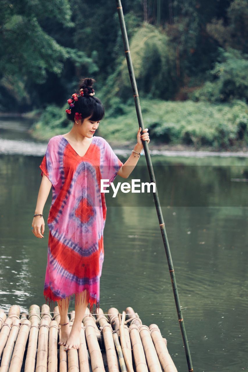 Woman holding bamboo while standing on wooden raft in lake