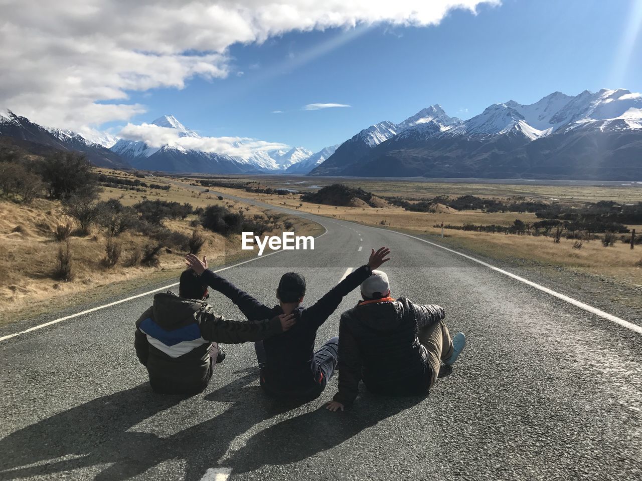 Rear view of men sitting on road against mountain range