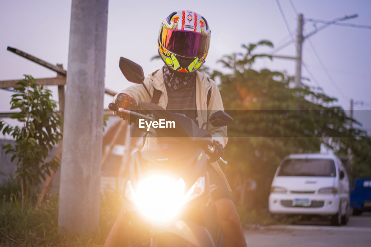 transportation, helmet, mode of transportation, headwear, one person, sports helmet, vehicle, car, nature, sports, adult, sports equipment, land vehicle, lens flare, sky, sunlight, men, adventure, crash helmet, motor vehicle, day, motorcycle, outdoors, road, clothing, extreme sports, protection, young adult, travel, leisure activity