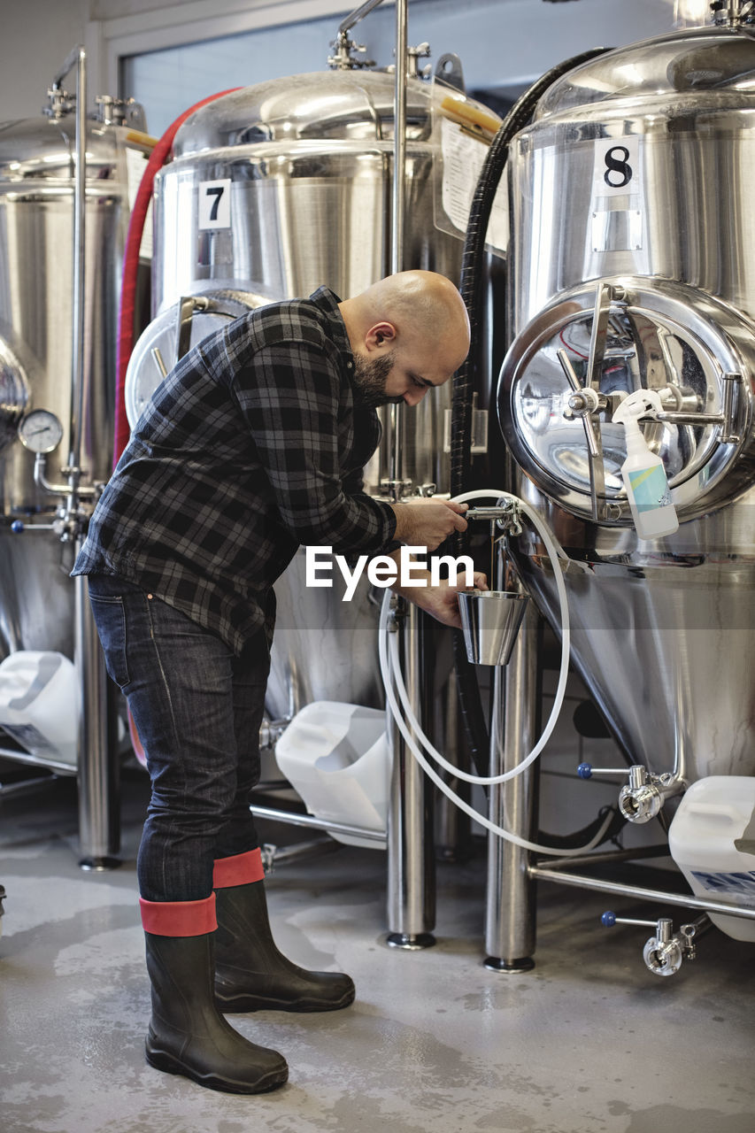 Full length of manager working by storage tank at brewery
