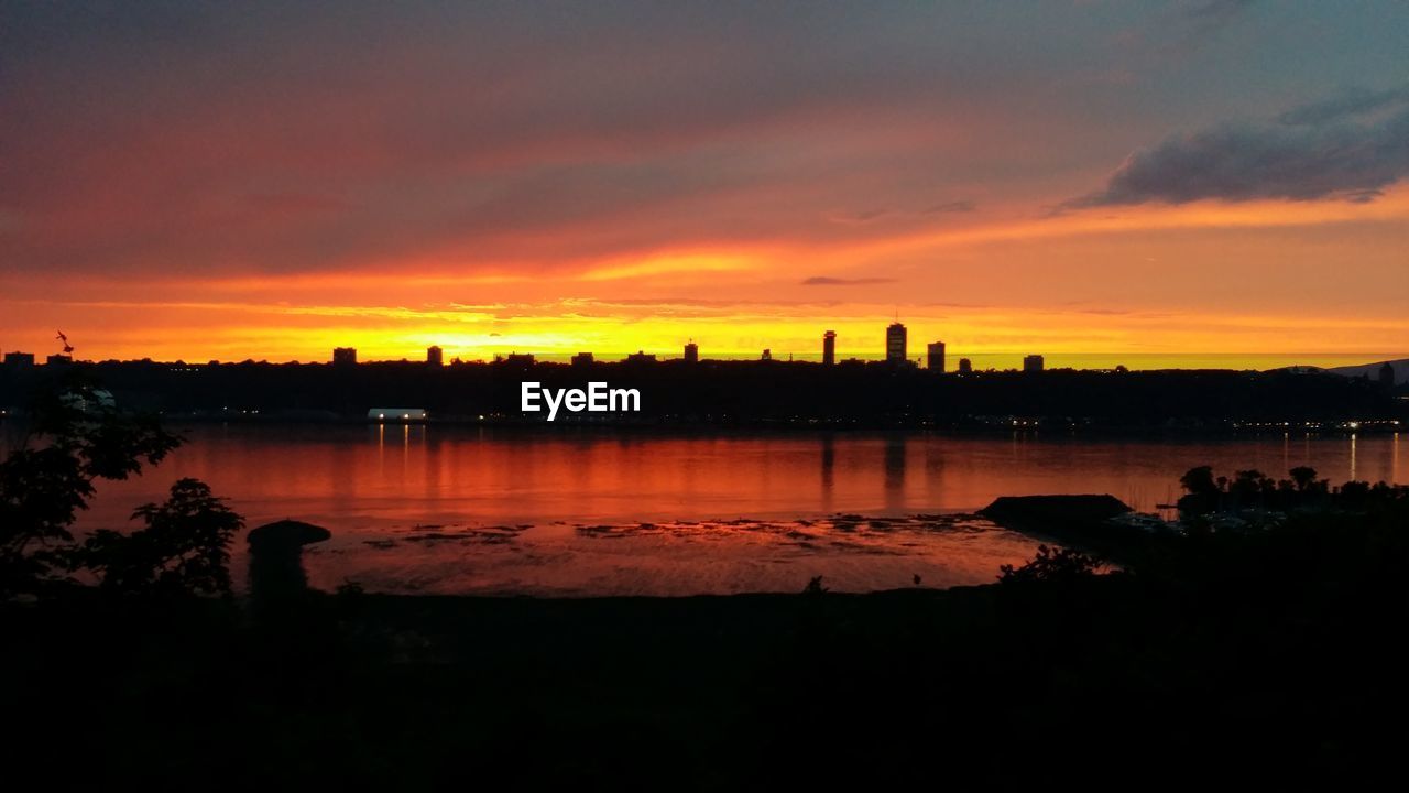 SILHOUETTE BUILDINGS BY LAKE AGAINST SKY DURING SUNSET