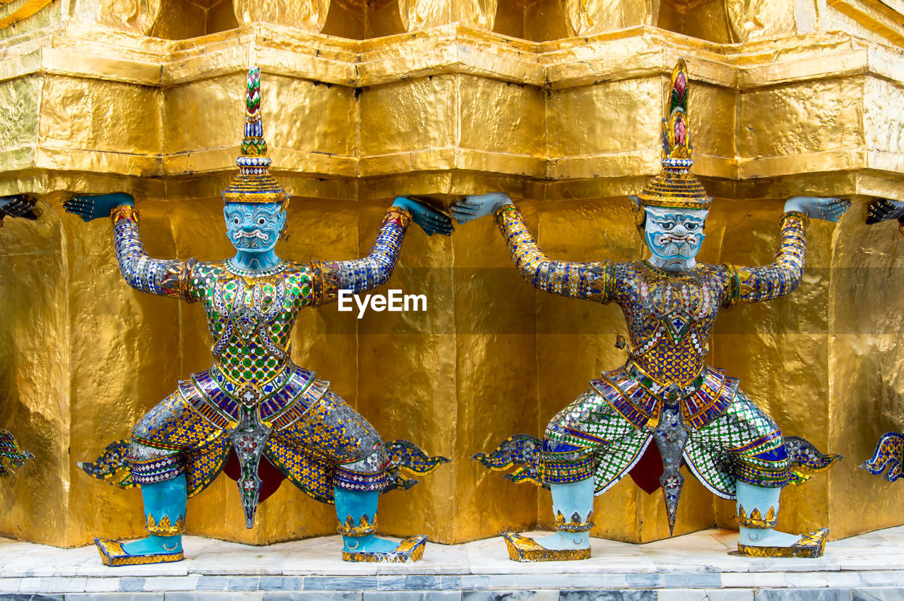 Close-up of demon statue against gold wall at wat phra kaew