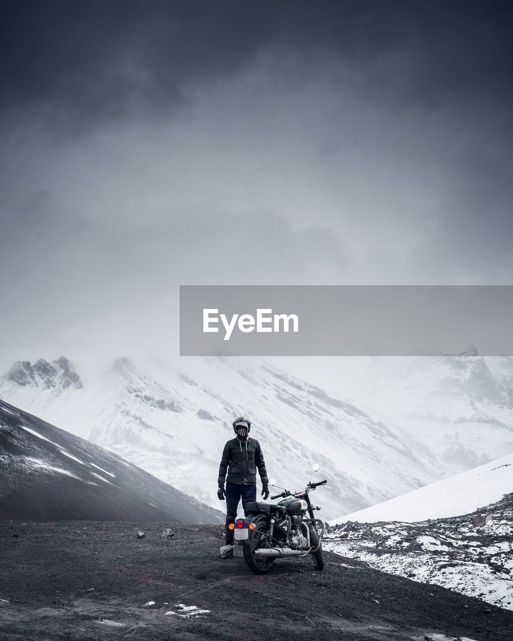 Man standing by motorcycle on road against snowcapped mountains