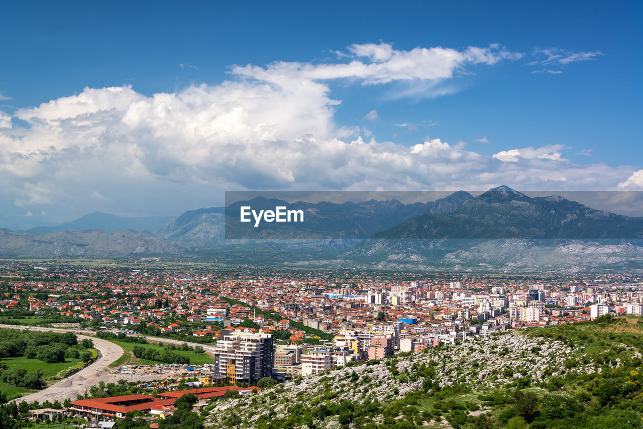 HIGH ANGLE VIEW OF TOWNSCAPE BY MOUNTAINS AGAINST SKY