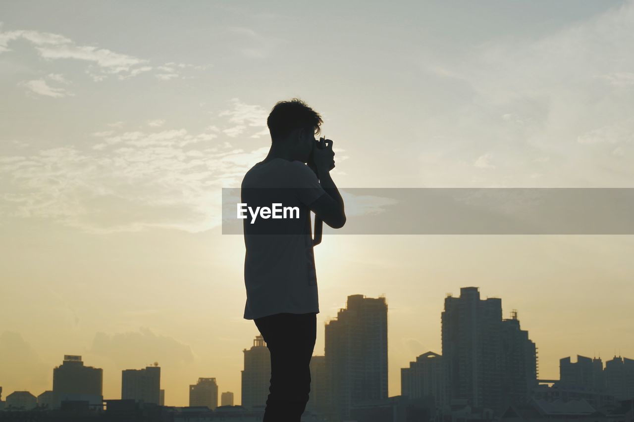 Man photographing standing in front of buildings during sunset