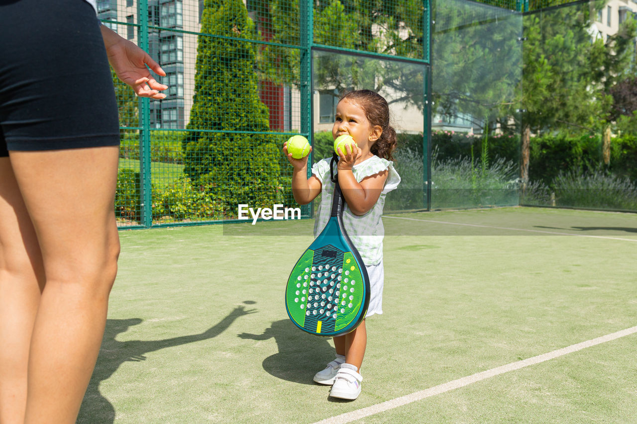 Little girl handing tennis balls to her mother on a padel tennis court