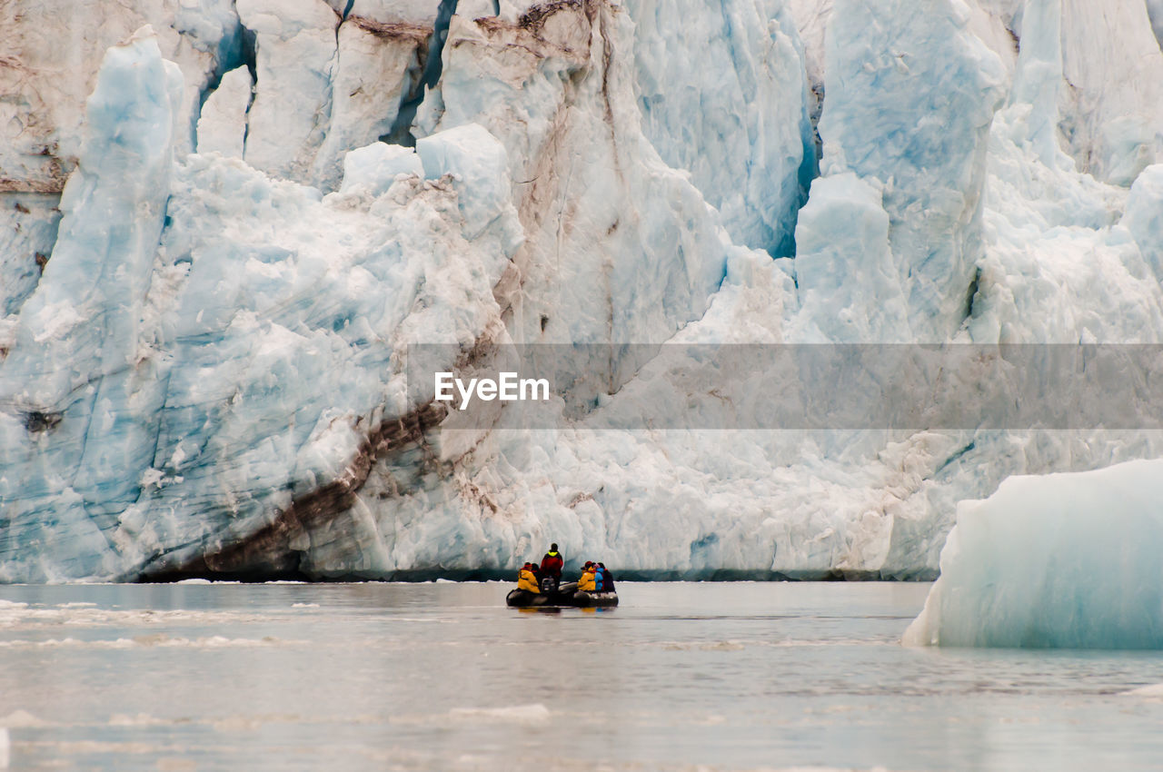 People on raft in sea against glacier