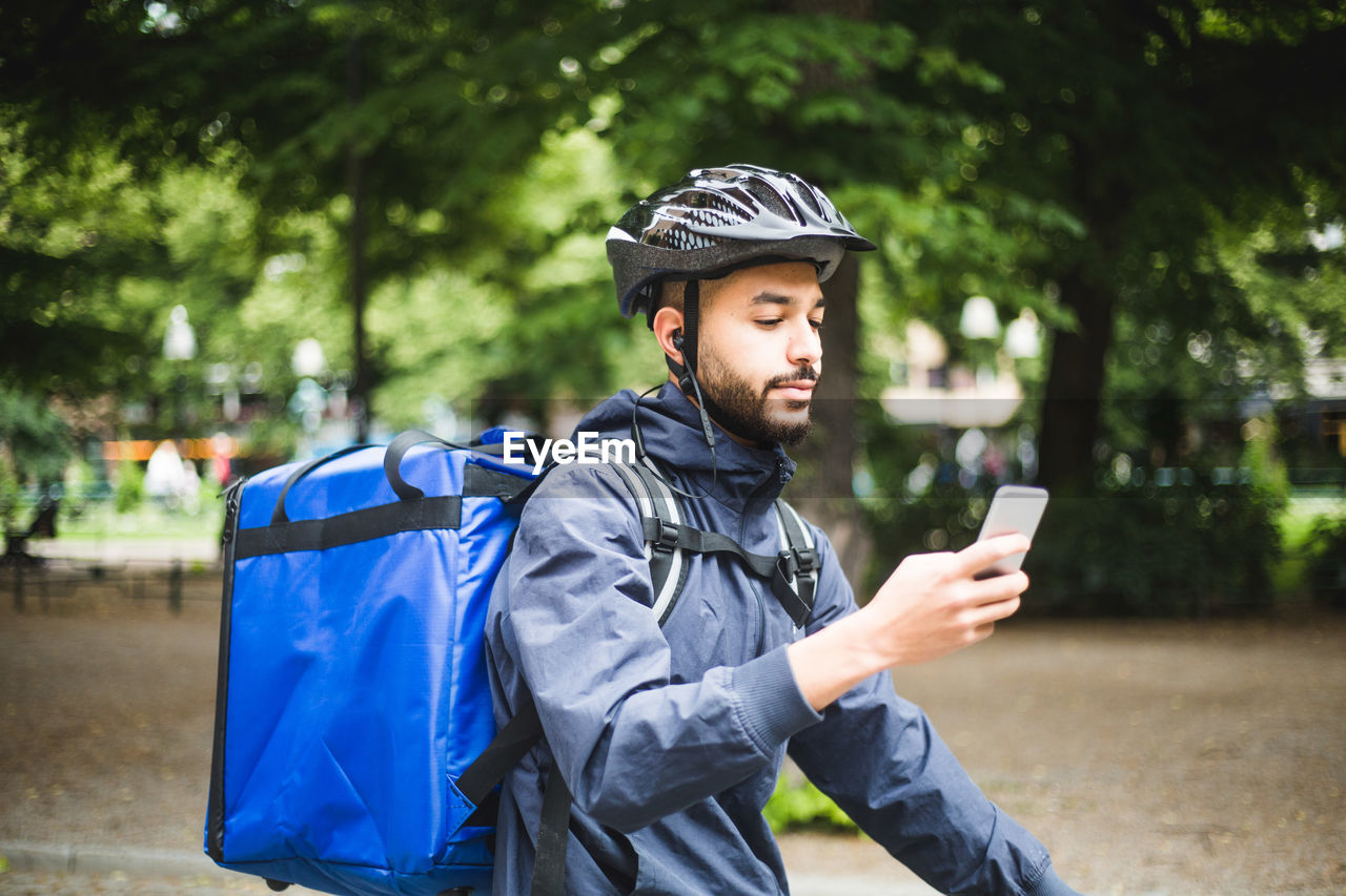 Food delivery man using smart phone on street in city