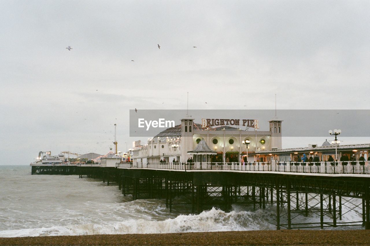 Brighton pier at beach against cloudy sky