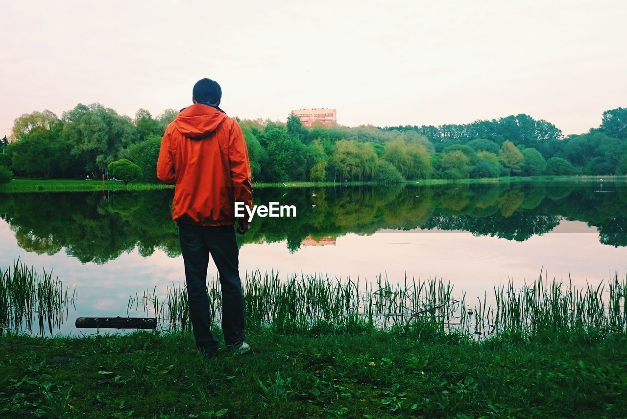 REAR VIEW OF MAN STANDING BY LAKE