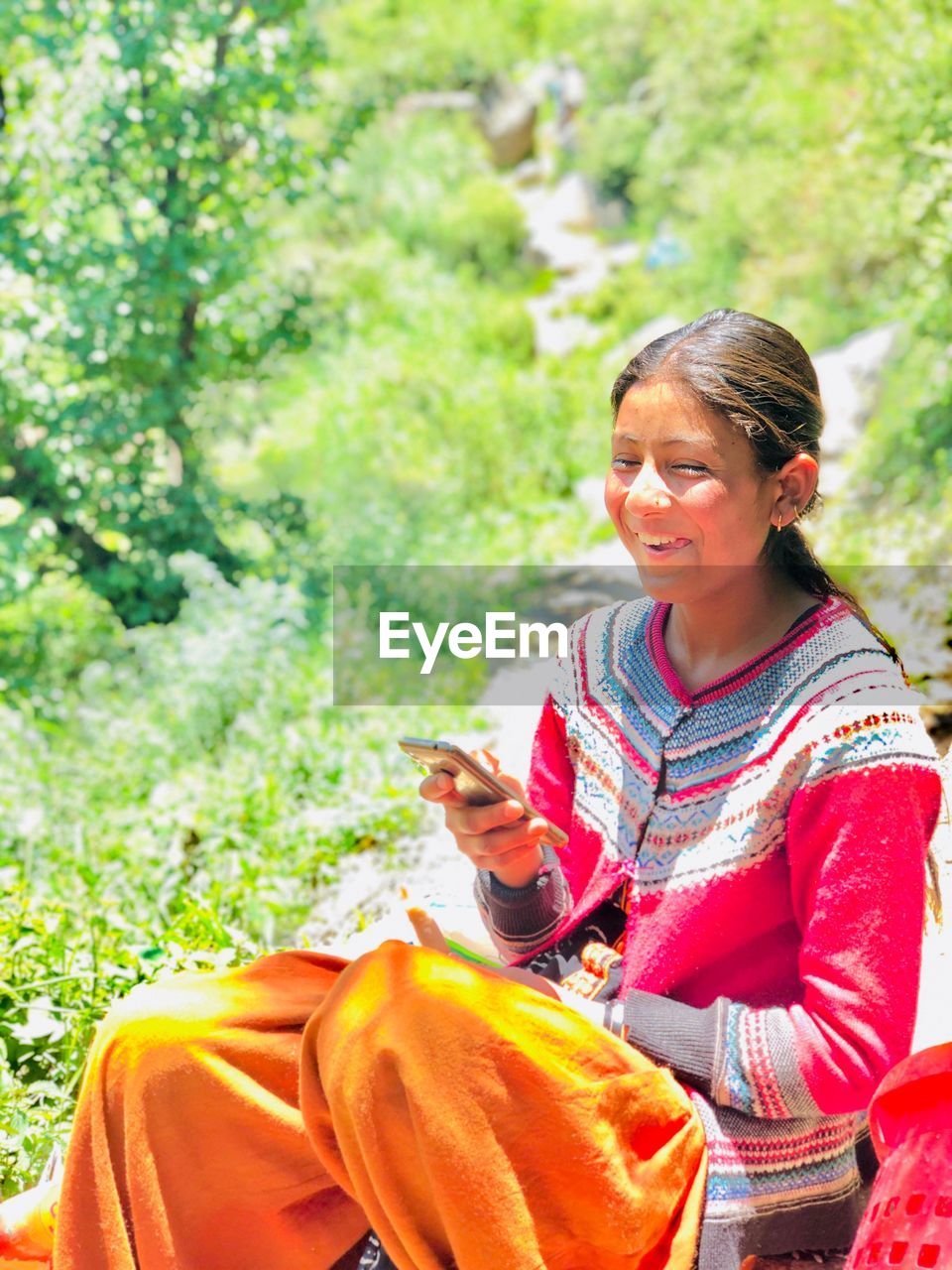 Smiling young woman using phone while sitting outdoors