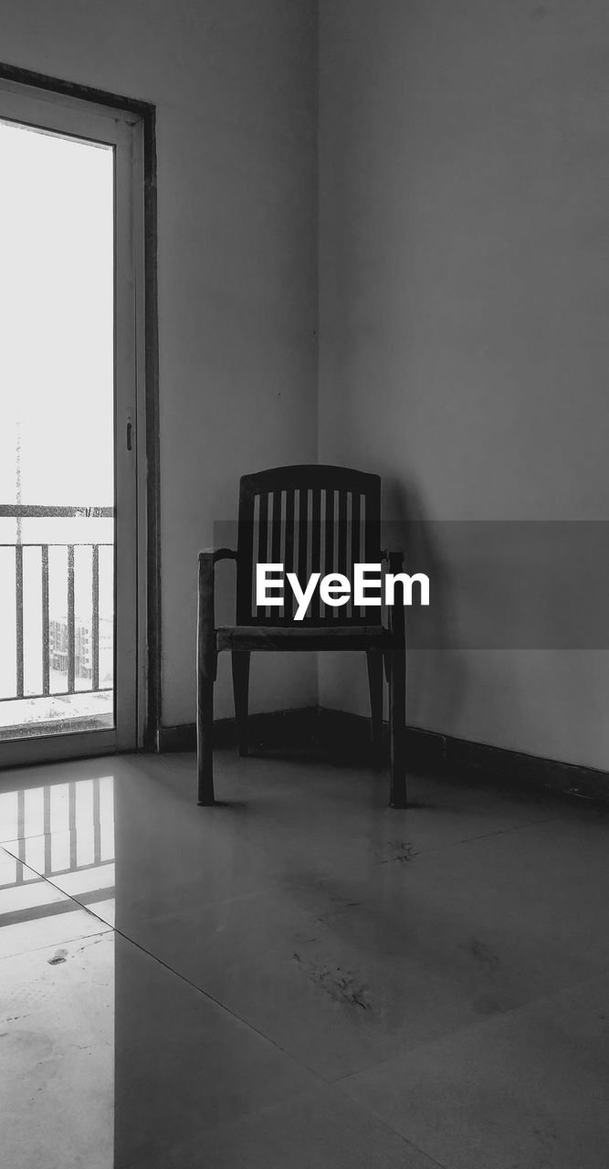 EMPTY CHAIR BY TABLE AGAINST WALL AT HOME