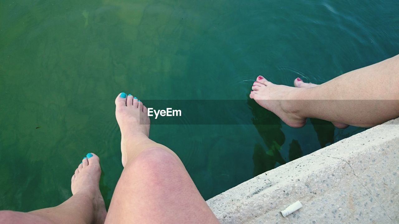 Low section of women sitting on pier over lake