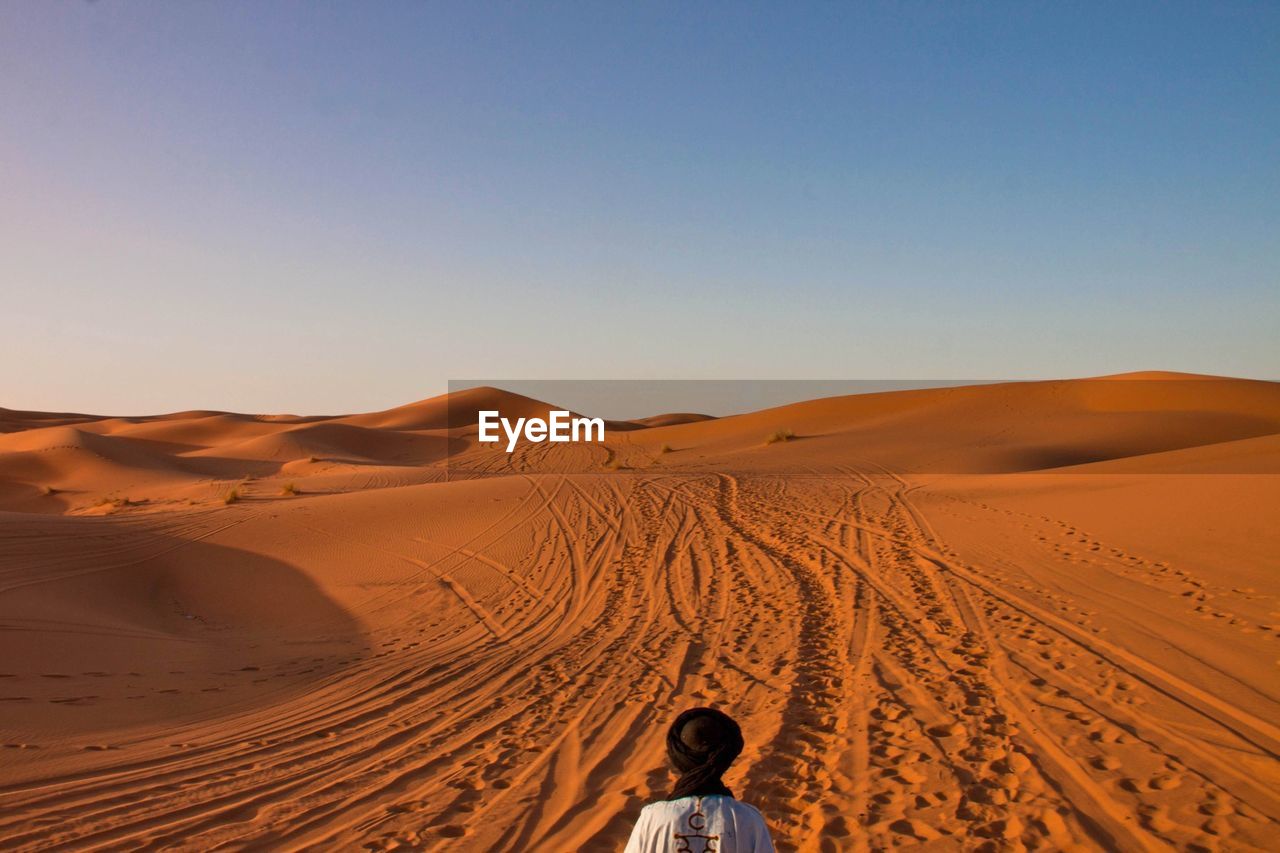 Rear view of man in desert against clear sky