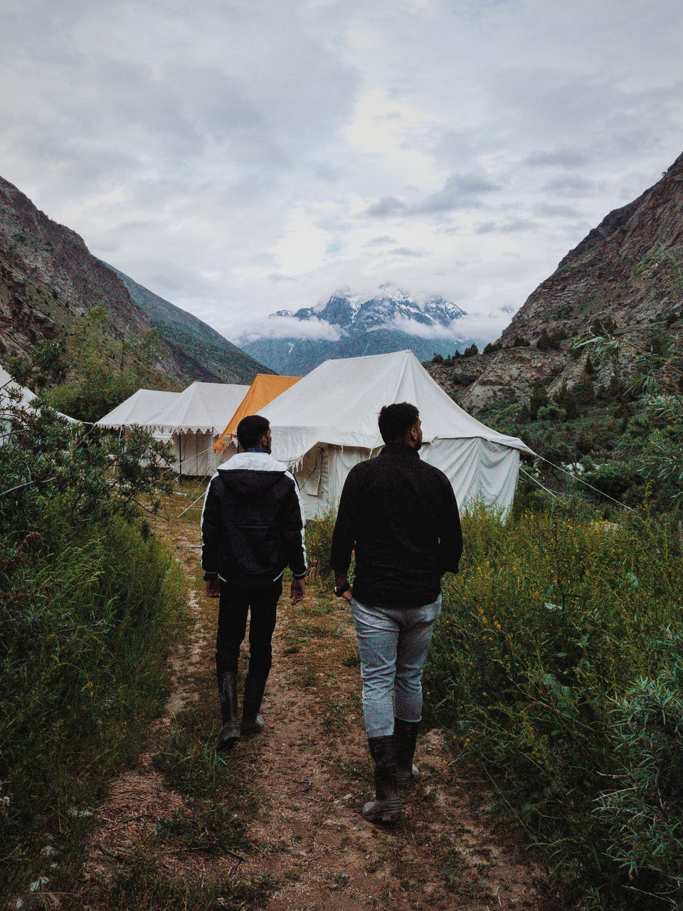 2 brothers walking down a valley camp site in ladakh overlooking majestic mountains and river