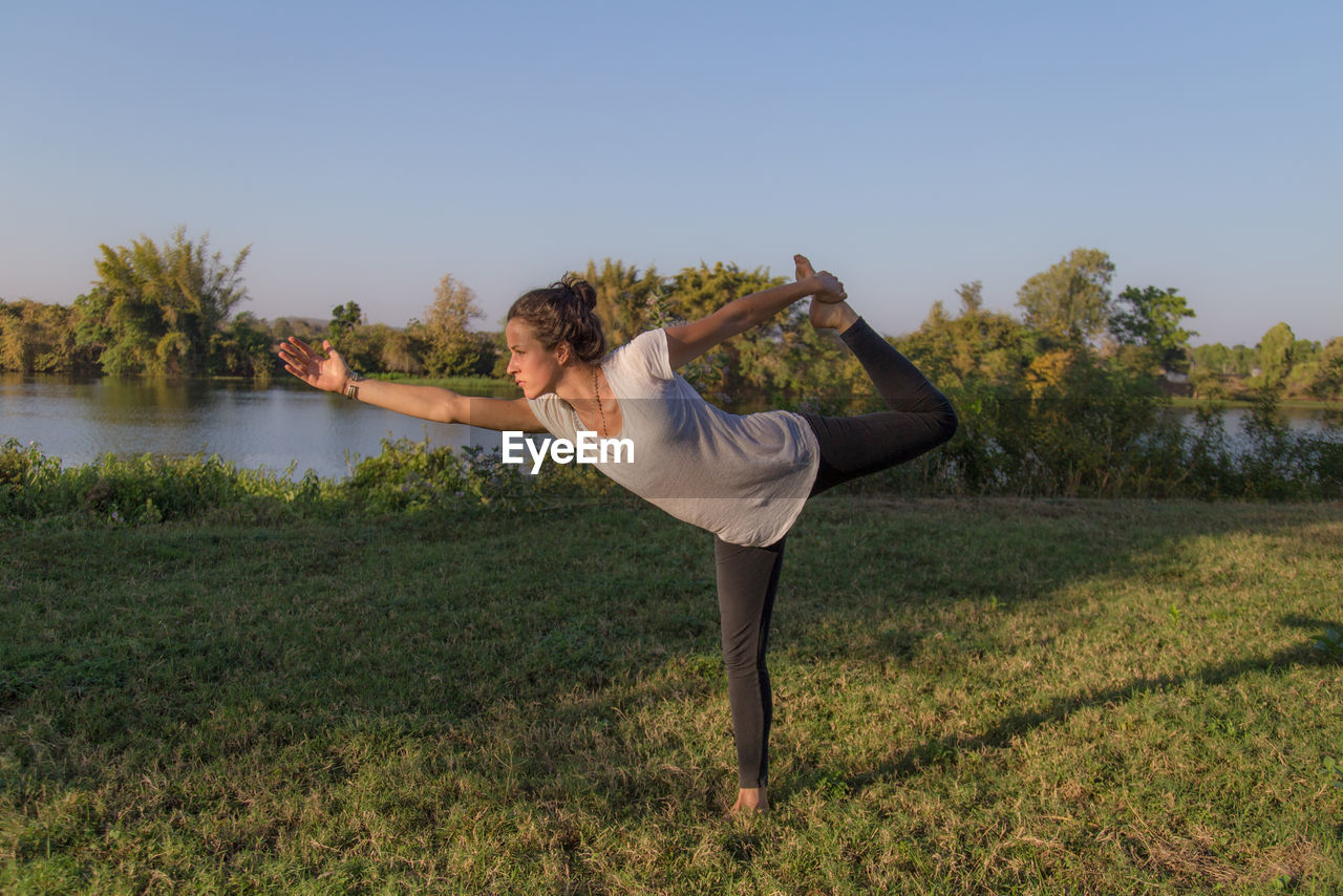 Beautiful woman practicing yoga on grass against blue sky during sunset