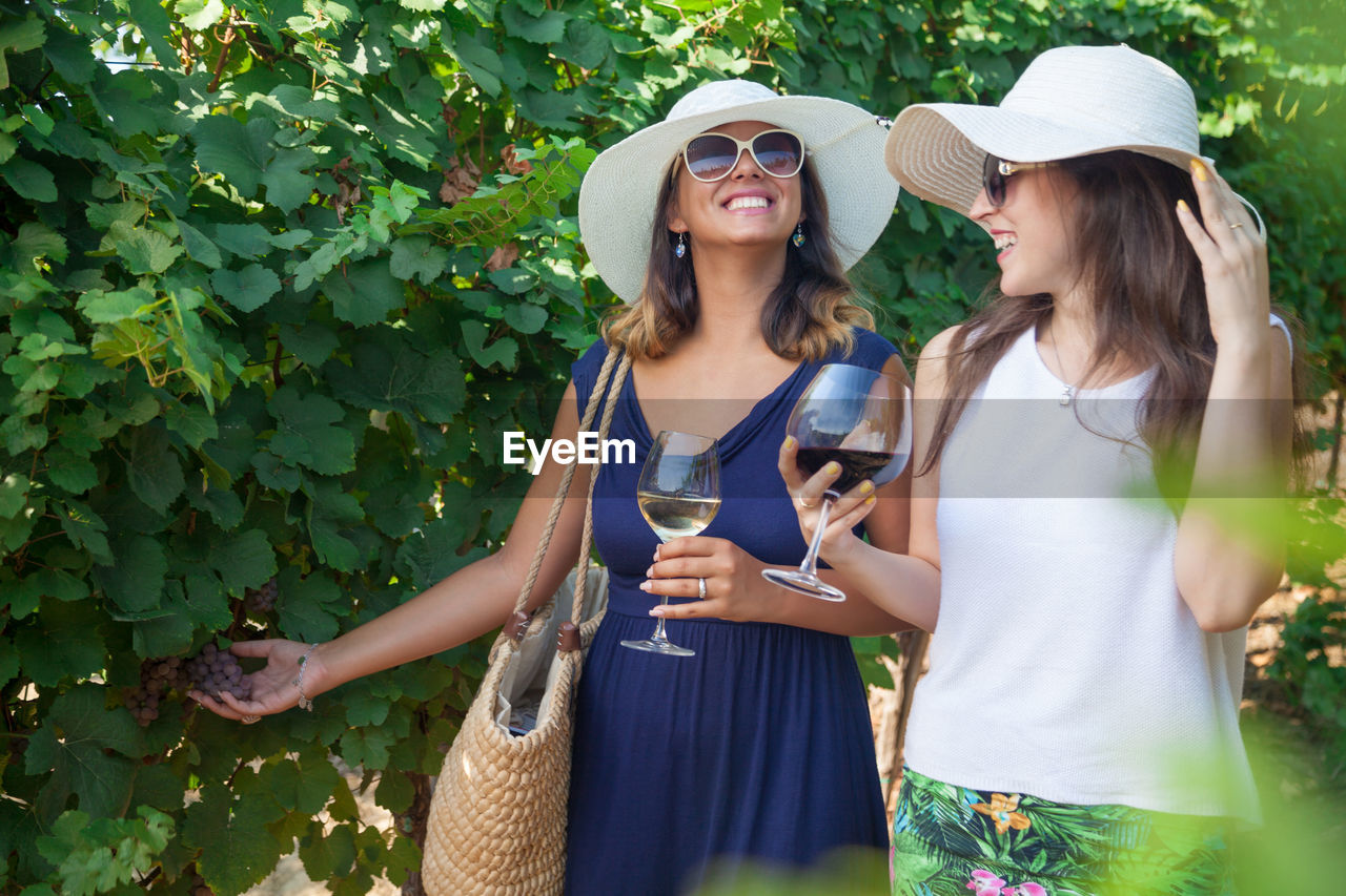 Young women drinking wine while walking by plants