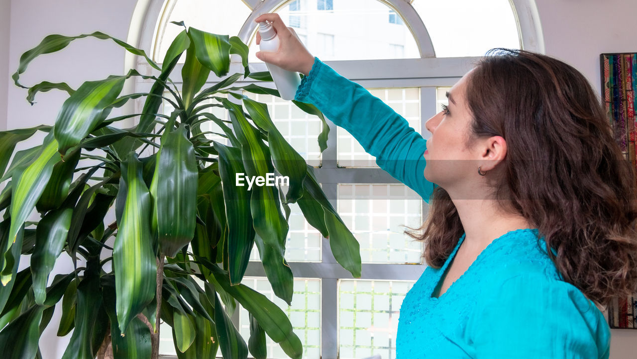 WOMAN LOOKING AWAY WHILE STANDING AGAINST PLANTS