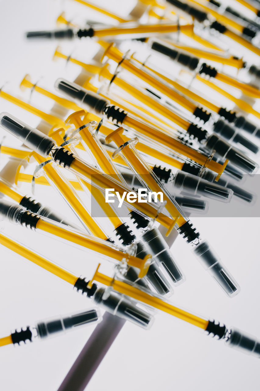 High angle view of yellow syringes against white background