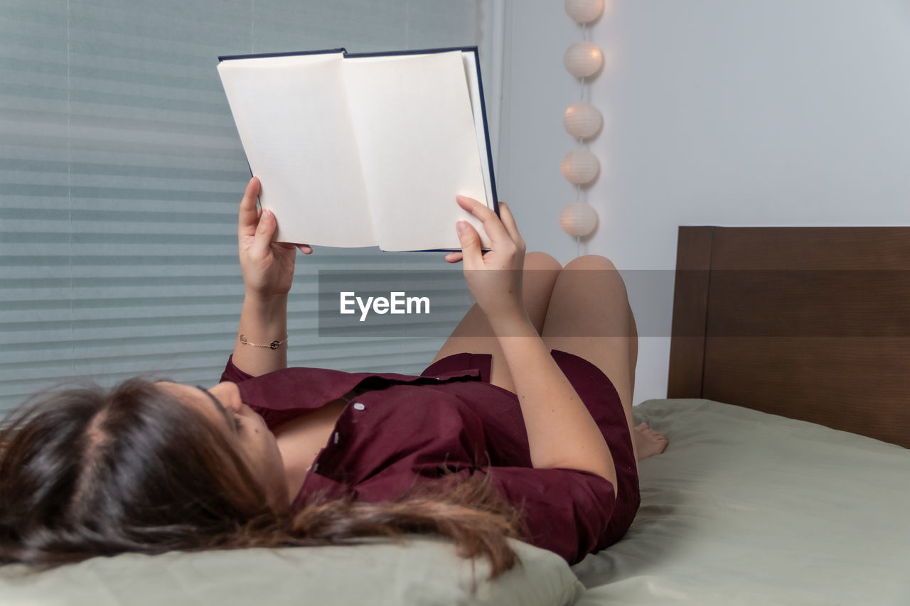 High angle view of woman reading book while lying on bed at home