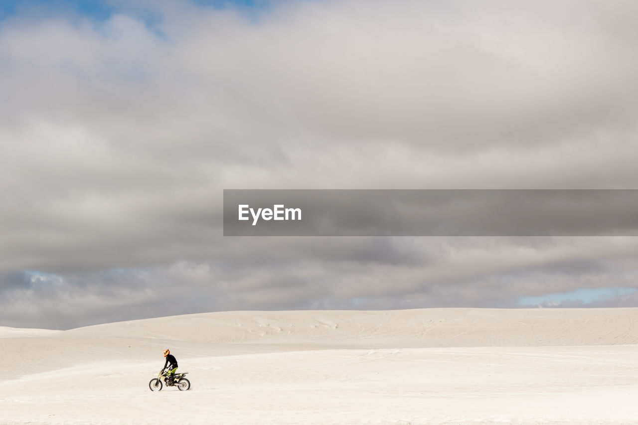Man riding motorcycle on sand against cloudy sky