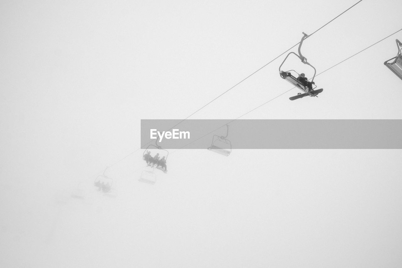 Low angle view of ski lifts against sky during foggy weather
