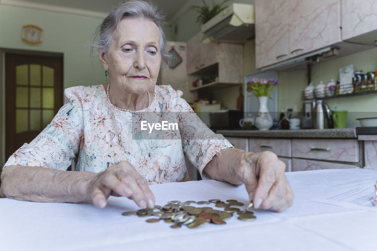 Senior woman counting savings on table at home