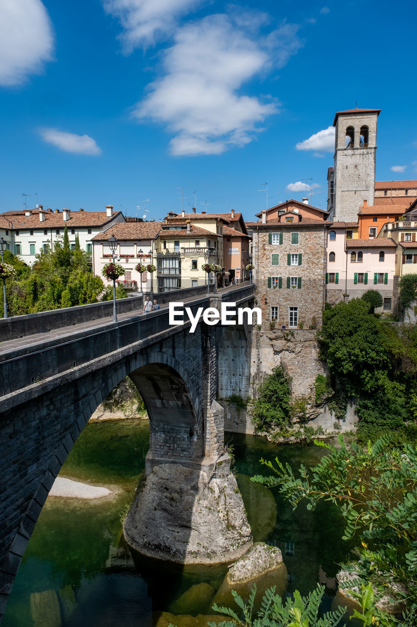 Arch bridge over river amidst buildings against sky