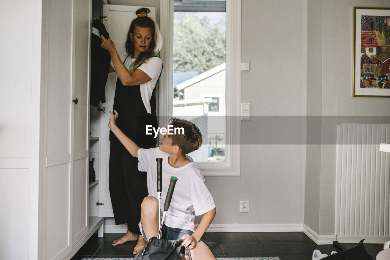 Son talking with mother standing by closet at home