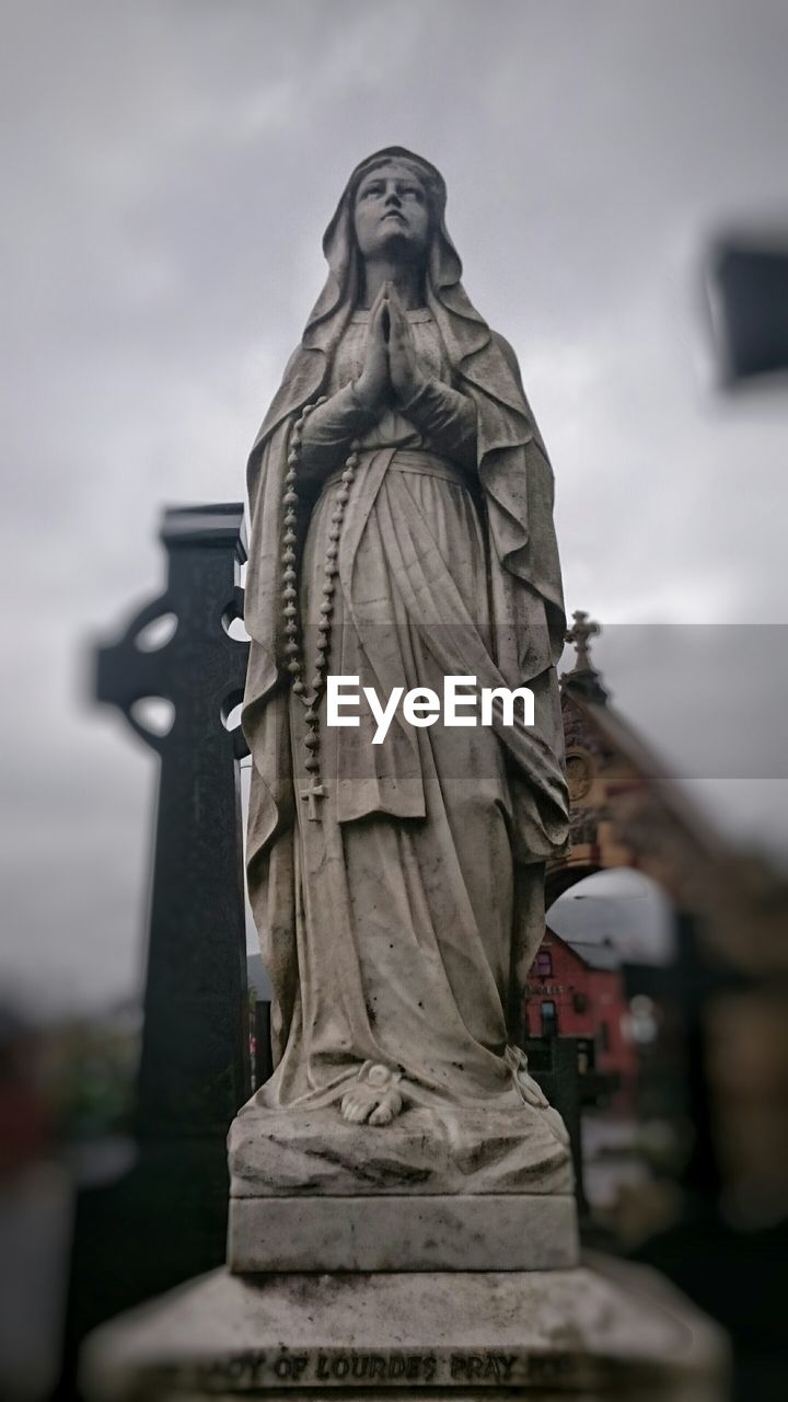 Statue of mother mary with hands clasped in cemetery