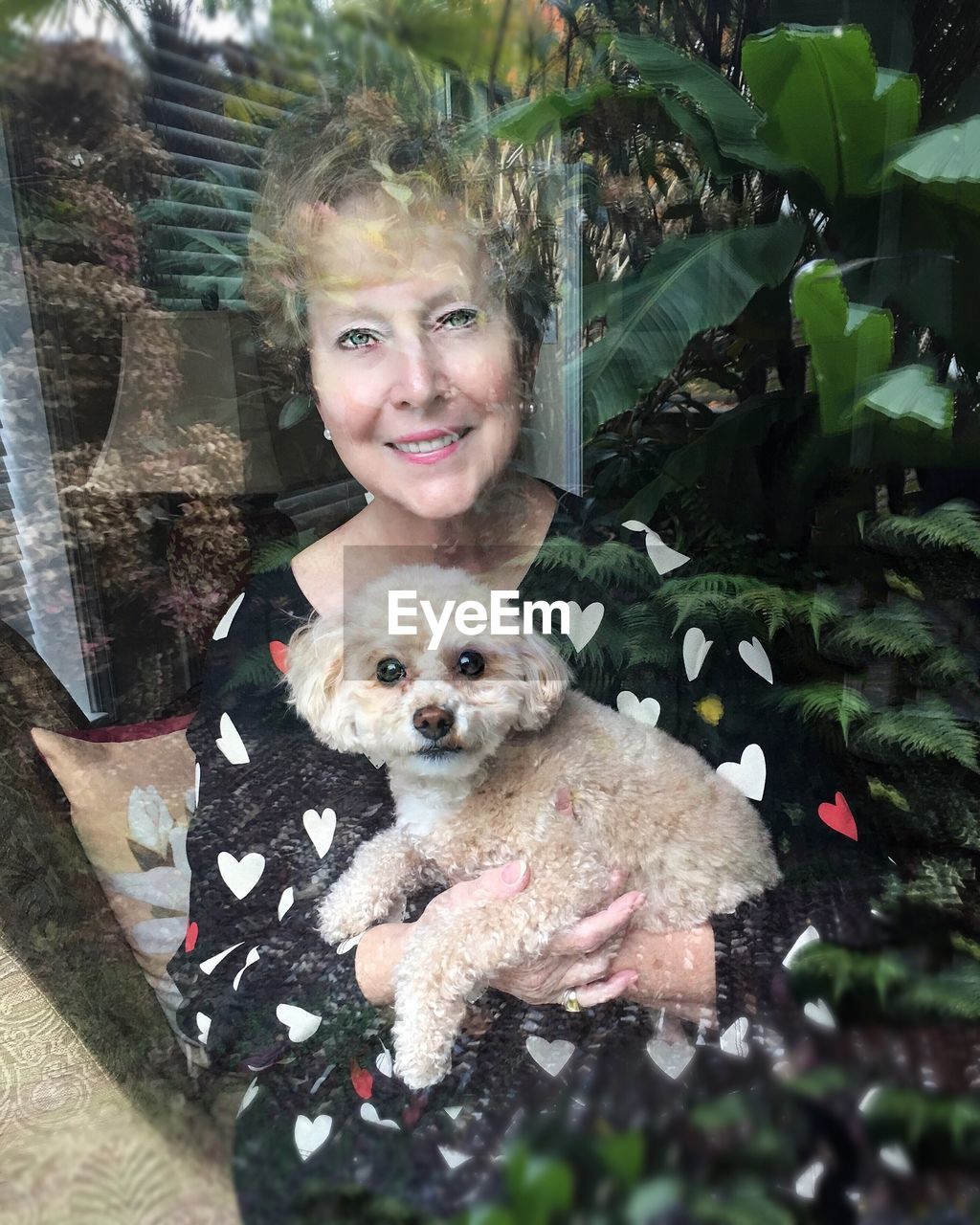 Portrait of smiling mature woman holding dog seen through glass window