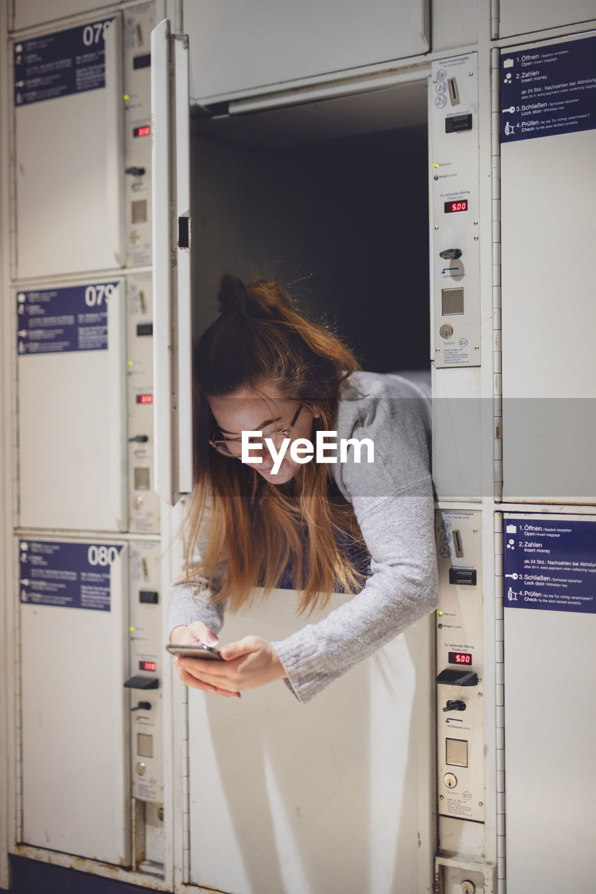 Young woman using phone in locker