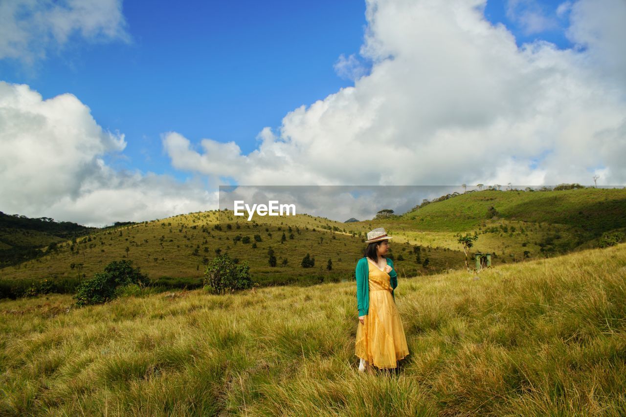 Mid adult woman standing on green landscape against sky