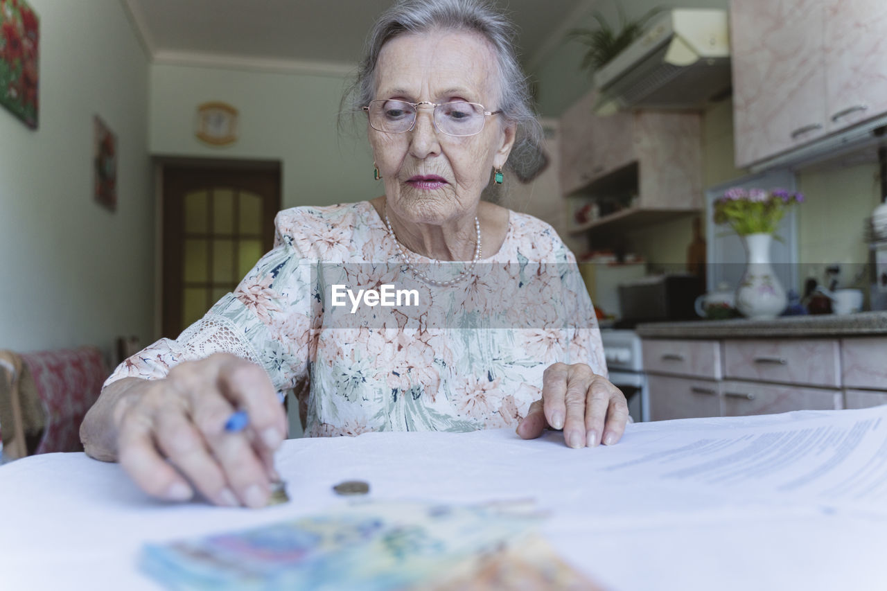 Senior woman with eyeglasses counting money on documents at home