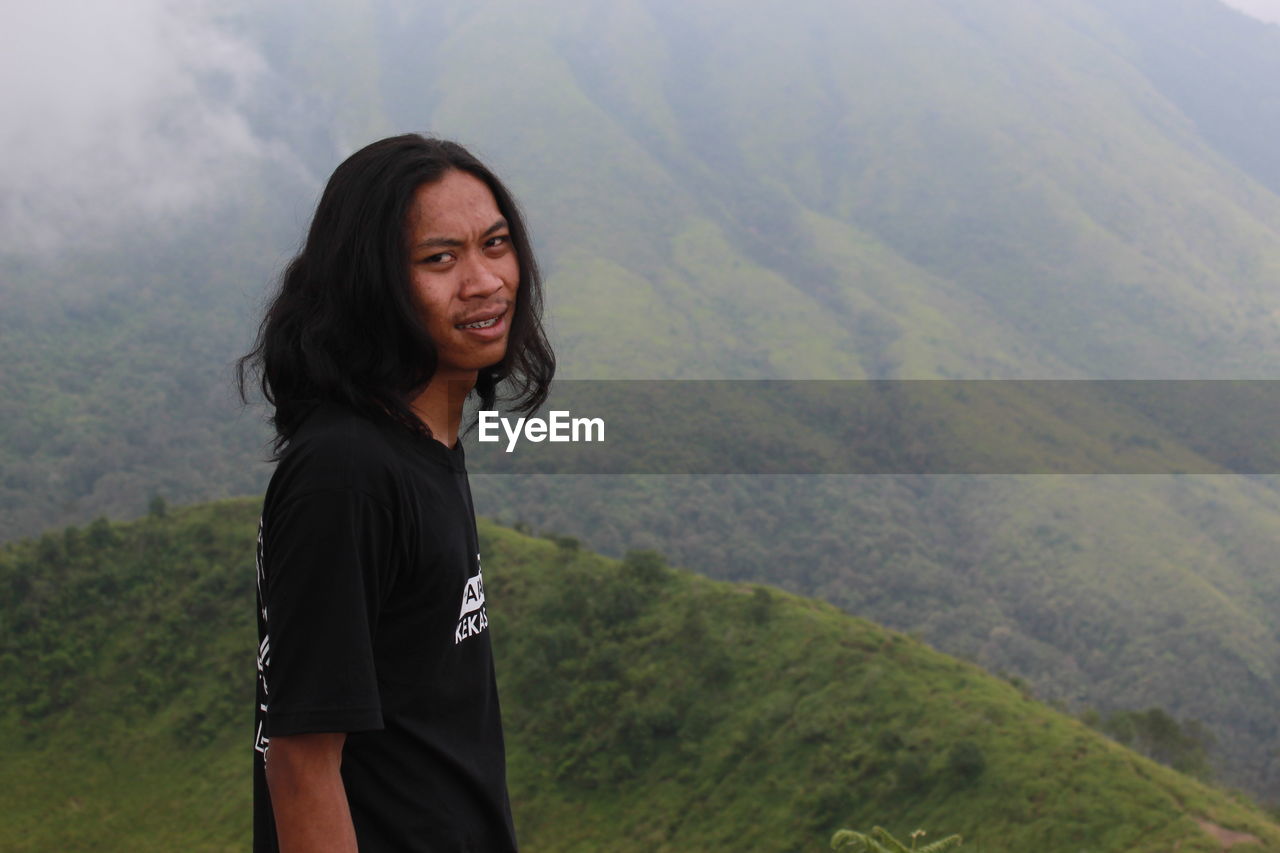 Portrait of beautiful young woman standing on landscape against mountains